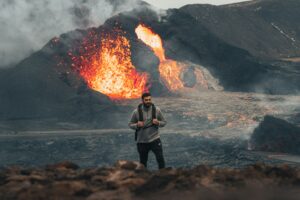 Photo d’un homme en train de marcher avec un sac à dos, près d’un volcan en éruption. Illustration du billet : Aaaah, la méditation.