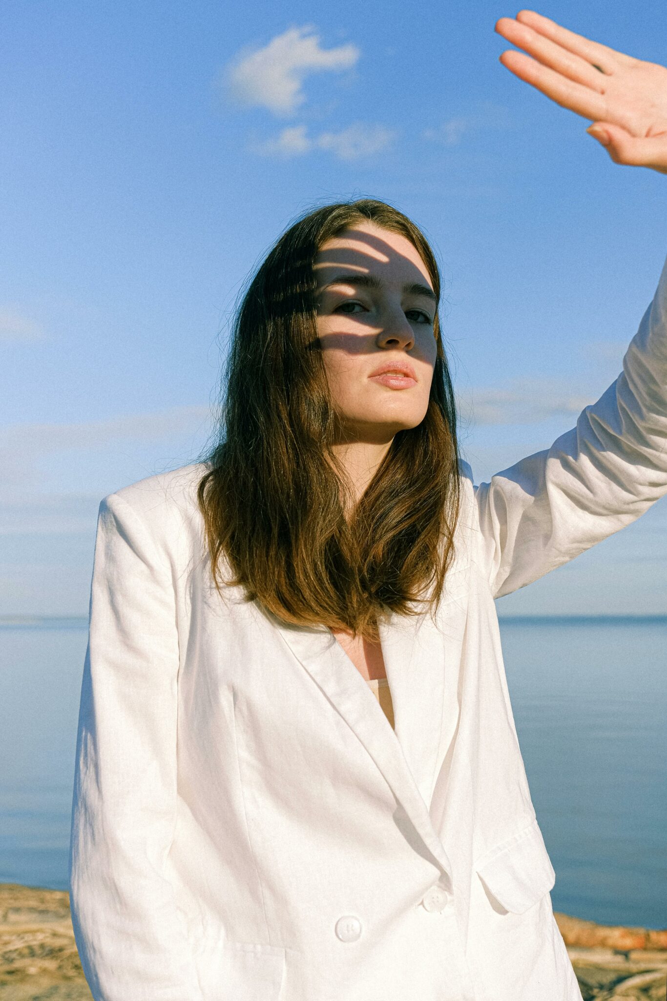 Une femme nous regarde, le bras levé pour se protéger de l’éblouissement du soleil. L’ombre de la main apparaît sur son regard. Illustration de l'émission : La zététique rend-elle insensible ?, du podcast Méta de Choc.