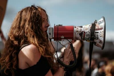Photo d’une femme calme avec un mégaphone en pleine manifestation. Illustration du chapitre 2 de l’émission : Trop militant•e pour être honnête ?, du podcast Méta de Choc. Ce chapitre s’intitule : Identifier nos biais cognitifs et les déjouer.