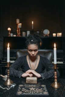 Photo d’une femme medium, face à nous, qui nous fixe, le regard entre deux bougies. Illustration du teaser de l’émission : Medium ou mentaliste, du podcast Méta de Choc.
