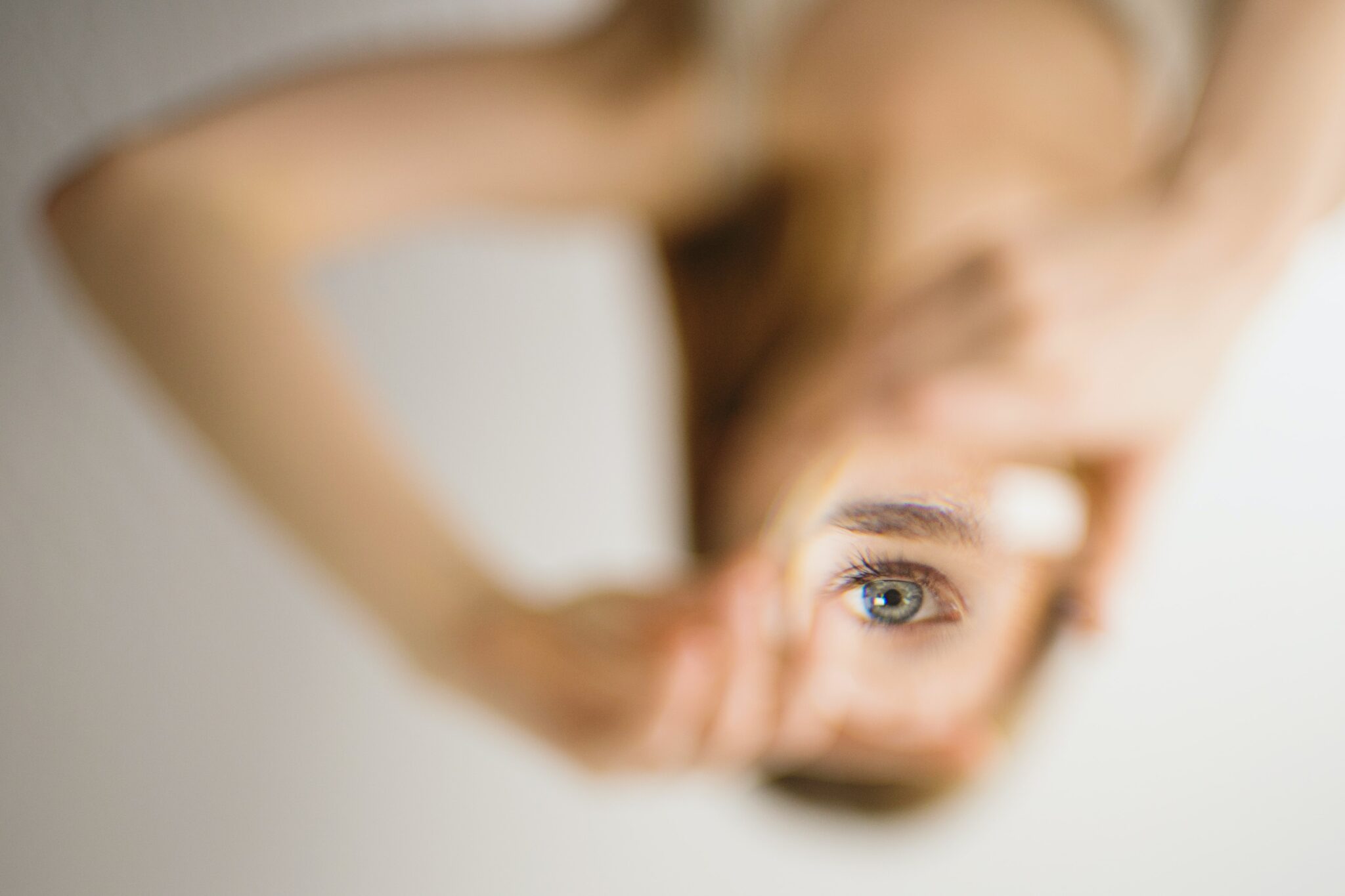 Photo d'une femme dont l'oeil nous observe dans un coin de miroir. Ses deux mains forment un cadre à travers lequel elle passe son regard.