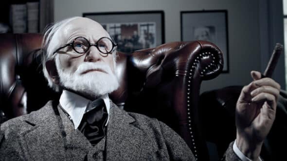 Androïde représentant Sigmund Freud, pensif, assis dans un fauteuil, le regard levé vers le ciel, pensif.