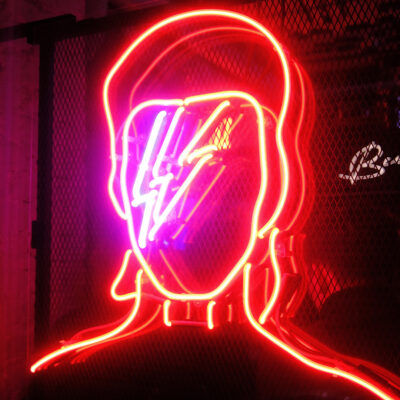 Illustration de la tête de David Bowie avec un éclair peint sur la figure, sous forme de néons de couleurs.