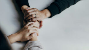 Deux paires de mains se tiennent et s'enlacent sur une table blanche. Illustration du teaser de l’émission STREAM intitulée : Santé mentale : fausses promesses et solutions, du podcast Méta de Choc.