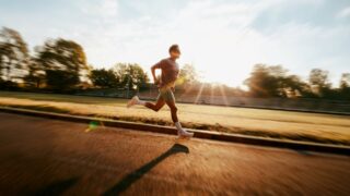 Un homme court sur une piste d’athlétisme en plein jour, avec le soleil en arrière plan. Illustration du Shocking intitulé « Les croyances dans le sport » du podcast Méta de Choc.