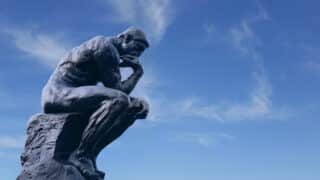 Sculpture du Penseur d'Auguste Rodin. La statut représente une réflexion profonde. En arrière-plan on peut voir un ciel bleu clair. Illustration du teaser de l’émission SHOCKING intitulée : L’esprit critique, ça s’apprend ? du podcast Méta de Choc.